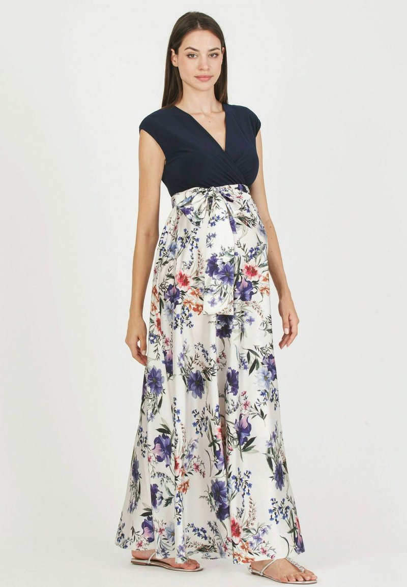 Robe de maternité avec un haut bleu marine et une jupe évasée en blanc, ornée de fleurs violettes, roses et bleues, avec un détail de nouage à l'avant.