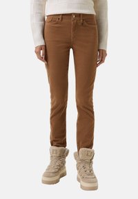Braune Cordhose mit taillierter Passform, ausgestattet mit einem Knopfverschluss und Fronttaschen, kombiniert mit beigefarbenen, mit Fleece gefütterten, klobigen Stiefeln.