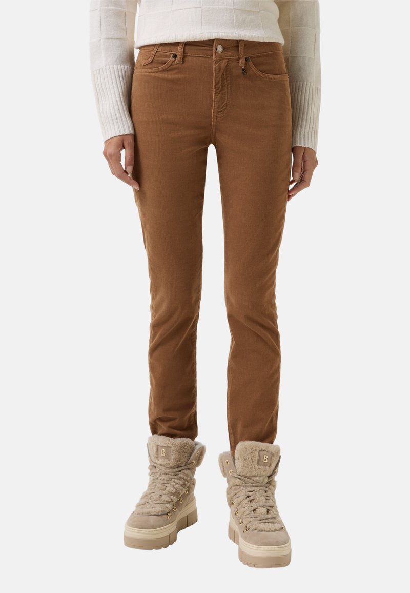 Braune Cordhose mit taillierter Passform, ausgestattet mit einem Knopfverschluss und Fronttaschen, kombiniert mit beigefarbenen, mit Fleece gefütterten, klobigen Stiefeln.