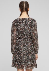 Black floral dress with long, sheer sleeves, elastic waist, and ruffled hem. Features multicolored flower patterns against a dark background.