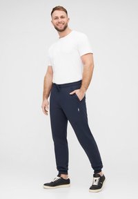Navy Jogginghosen mit elastischem Bund, seitlichen Taschen und einem dezenten Logo. Kombiniert mit einem kurzärmeligen weißen T-Shirt und schwarzen Sneakers.