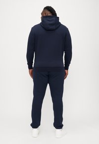 Ναυτικό μπλε φούτερ με κουκούλα και κορδόνι, συνδυασμένο με ταιριαστά παντελόνια φόρμας. Κατασκευασμένο από μαλακό υλικό, με ριμπ μανσέτες και τελειώματα ποδιών.