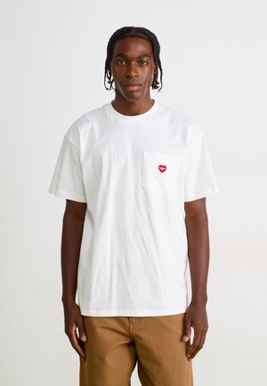 White cotton t-shirt with short sleeves, featuring a red heart logo on the left pocket. Simple design, relaxed fit, and soft texture.