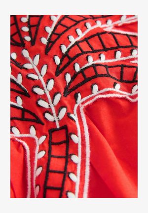 Roter Stoff mit komplizierter schwarzer und weißer Stickerei von Blatt- und geometrischen Mustern, mit strukturiertem Stich und kontrastierenden Farben.