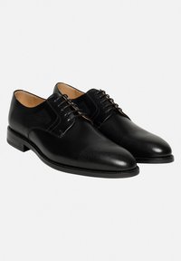 Chaussures en cuir noir à lacets avec une surface texturée comportant des motifs perforés, un bout arrondi et des accents polis sur le cap.