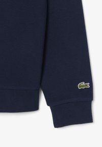 Marinblus långärmad skjorta med texturerad tyg, ribbade ärmslut och en liten grön krokodil-logotyp broderad på ärmen.