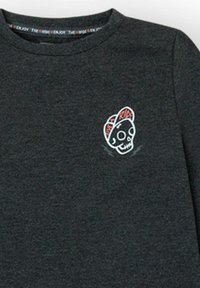 Camiseta de manga larga gris oscuro con escote redondo y un pequeño gráfico colorido de una calavera con gorra en el lado izquierdo del pecho.