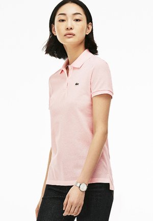 Polo in rosa chiaro con tessuto morbido, maniche corte, colletto e un piccolo logo sul lato sinistro del petto, abbinato a jeans scuri.