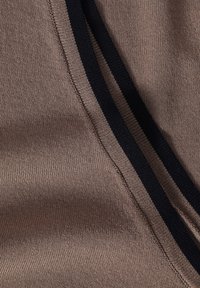 Pull en laine taupe avec des rayures bleu marine foncé. Caractérisé par une texture douce et des accents côtelés le long des bords. Design simple et épuré.