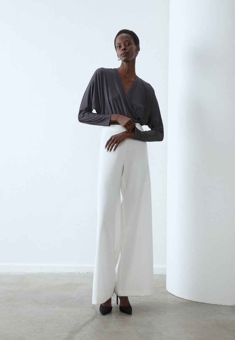 Szary top z długimi rękawami, połączony z białymi spodniami o szerokich nogawkach. Czarne czółenka na wysokim obcasie dopełniają nowoczesny, uporządkowany wygląd.