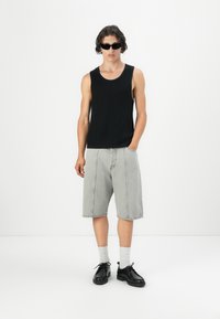 Sort ribbet tanktop parret med lysegrå knælange shorts; modellen bærer sorte solbriller og sorte sko med hvide sokker.