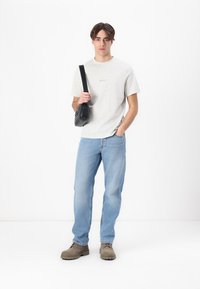 Light gray crew-neck t-shirt, blue straight-leg jeans, and brown shoes. Black crossbody bag with circular hardware detail. Simple, casual outfit.