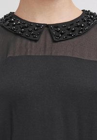 Top nero con una sezione trasparente, corpetto strutturato e colletto decorato con perline nere e paillettes.