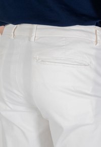 Pantaloni di cotone bianchi con una texture liscia, dotati di una tasca posteriore e passanti per cintura, mostrati da un'angolazione laterale su uno sfondo neutro.