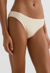 Teksturowane, kremowe majtki bikini o niskim stanie z wycięciami po bokach, zdobione subtelnym, pęcherzykowym wzorem na całej tkaninie.