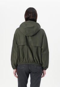 Casaco leve verde oliva com capuz, cintura elástica e textura suave. Apresenta um design de yoke na parte de trás.