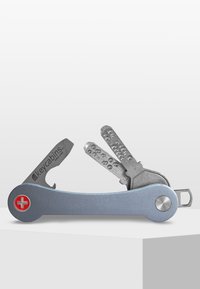 Multiverktyg nyckelhållare med en matt silverfärgad aluminiumkropp, röd korssymbol och metallnyckelinsatser med distinkta mönster för enkel åtkomst.