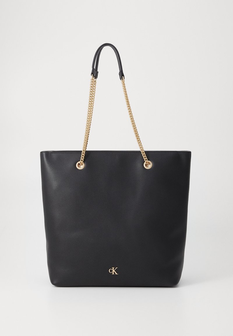 Sac cabas en cuir noir avec poignées chaîne dorée et petit logo doré « CK » à l'avant sur fond uni.