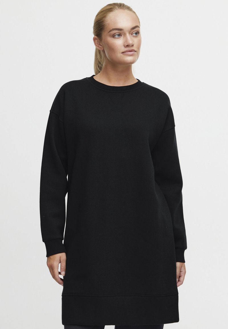Svart sweatshirtklänning, långärmad, med rund hals, avslappnad passform och ribbade muddar. Slät textur, knälång, minimal design.