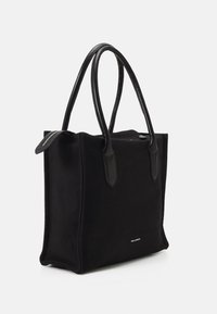 Black canvas tote bag with black leather handles, rectangular shape, zippered closure, flat base, and subtle logo detail on the front.