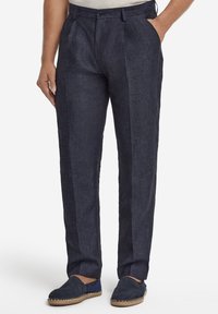 Marinblå linnebyxor med strukturerad yta, utrustade med framåtvikt, sidfickor och kombinerade med marinblå slip-on skor.