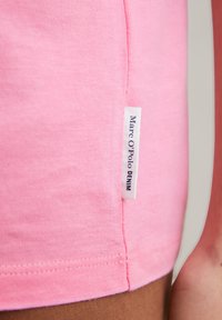 Rosa Baumwoll-T-Shirt mit glatter Textur, ausgestattet mit einem seitlichen Etikett, das "Marc O'Polo DENIM" trägt. Die Nähte sind ordentlich; es ist für die Freizeitgestaltung entworfen.