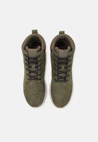 Stivali da trekking in suede verde oliva con inserti in pelle marrone, lacci neri e linguette imbottite. Progettati per il comfort con una superficie texturizzata.