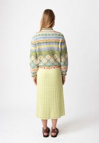 Ažūrinis megztinis su daugiaspalviais geometriniais raštais, derinamas su pastelinės žalios spalvos riboto ilgio sijonu. Rudi sandaļa su dirželiais užbaigia įvaizdį.