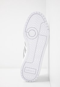 Vit sportskosula med texturerat greppmönster, prydd med tre grå ränder, släta kanter och en präglad Adidas-logotyp.