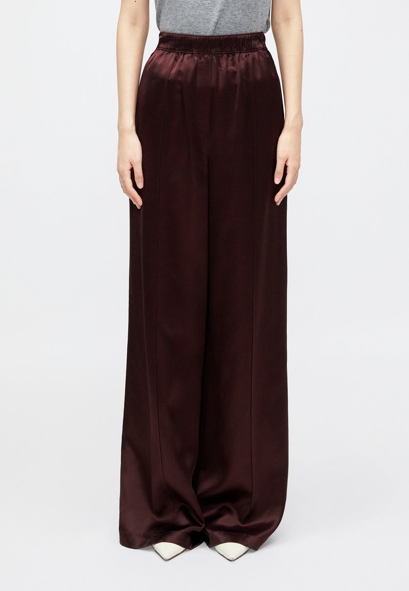 Bordo široke hlače iz satenskega materiala z elastičnim pasom, s papirjem vertikalnimi šivi in gladko, sijočo teksturo.