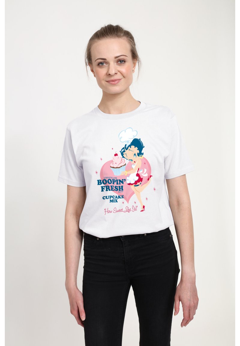 Hvid bomulds t-shirt med et farverigt cartoon-graphic af en karakter med blåt hår, der holder en cupcake, samt tekstelementer i pink og blå.