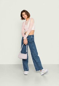 Top cropped rosa de mangas longas, jeans de perna reta de cintura alta em denim, sapatilhas brancas e uma pequena mala lilás. Texturas suaves, design casual.