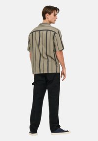 Short-sleeve shirt in light olive with vertical dark stripes, paired with black cargo pants. Material appears textured. Casual style.