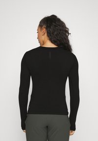 Black long-sleeve athletic top with a fitted design, smooth texture, and subtle seam detailing on the back, paired with olive green pants.