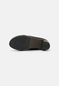 Suela de zapato negra con textura en el dibujo, tacón elevado y el nombre de la marca "SOFTCLOX" en relieve, fotografiado sobre un fondo blanco.
