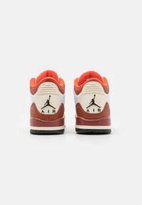 Sneaker bianca e arancione con tacco marrone testurizzato, dotata di logo "Air" nero e Jumpman; collo imbottito e suola in gomma.