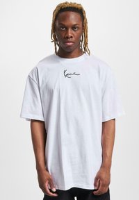 White cotton t-shirt with a relaxed fit, features a black handwritten logo on the chest, short sleeves, and a round neckline.