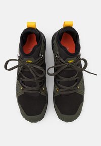 Scarpe nere e verde oliva con tomaia in rete, lacci rotondi, colletto imbottito e un'etichetta gialla; suola testurizzata per una migliore trazione.