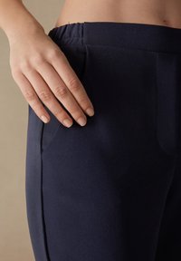 Pantaloni in tessuto elasticizzato blu navy con cintura elastica e tasche laterali, caratterizzati da una trama liscia e una vestibilità sartoriale.