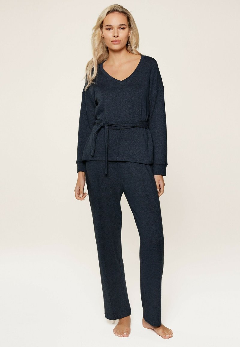 Completo loungewear blu scuro che presenta una maglietta con scollatura a V e cintura annodata, insieme a pantaloni a vestibilità ampia, realizzati in un tessuto texturizzato.