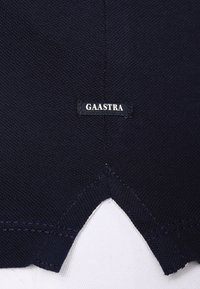 Tissu en coton bleu marine avec une finition texturée ; présente une étiquette blanche "GAASTRA" cousue sur un ourlet en forme de V au bas.