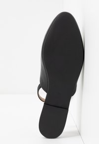 Semelle de chaussure noire vue de face avec la taille 37 embossée, une semelle minimaliste et un talon bas, sur un fond blanc en coin.