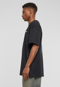 Sort bomulds t-shirt med korte ærmer, der har en rund halsudskæring og et grafisk print på ryggen. Lige snit, afslappet pasform.