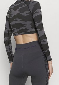 Getailleerde lange mouwen top in zwart en grijs camouflagemotief, gecombineerd met hoge taille grijze leggings met geribbelde textuur en een logo-opdruk op de tailleband.
