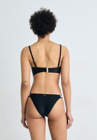 Set di bikini nero con spalline sottili e una chiusura sul retro, con un design senza cuciture e sottili accenti dorati sulla banda.