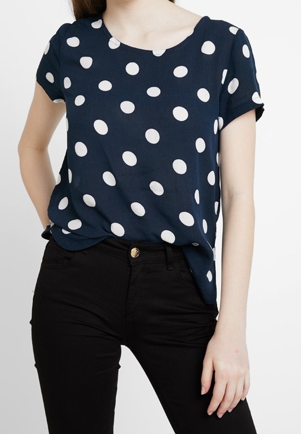 Blå topp med prickar i lätt tyg, med vita cirkulära mönster, korta ärmar och rund halsringning, paired med svarta byxor.