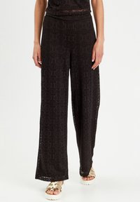 Schwarze weite Hosen aus strukturierter Spitze mit einem eleganten kreisförmigen Muster. Mit einem elastischen Bund und weit geschnittenen Beinen.