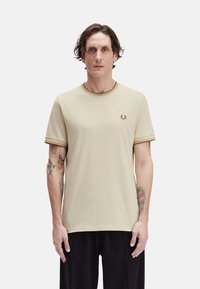 Camiseta de algodón beige con mangas cortas, cuello y puños de manga acanalados en marrón en contraste, con un pequeño logo bordado en el pecho.