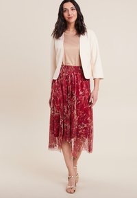 Rode bloemen midi-rok met een geplooid ontwerp, elastische tailleband; gecombineerd met een beige top en een crèmekleurige blazer. Gouden sandalen maken de look compleet.