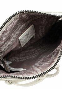 Interiér bílé tašky obsahuje kapsu na zip. Podšívka je hnědá s bílým textem a zip má černé zuby pro kontrast.